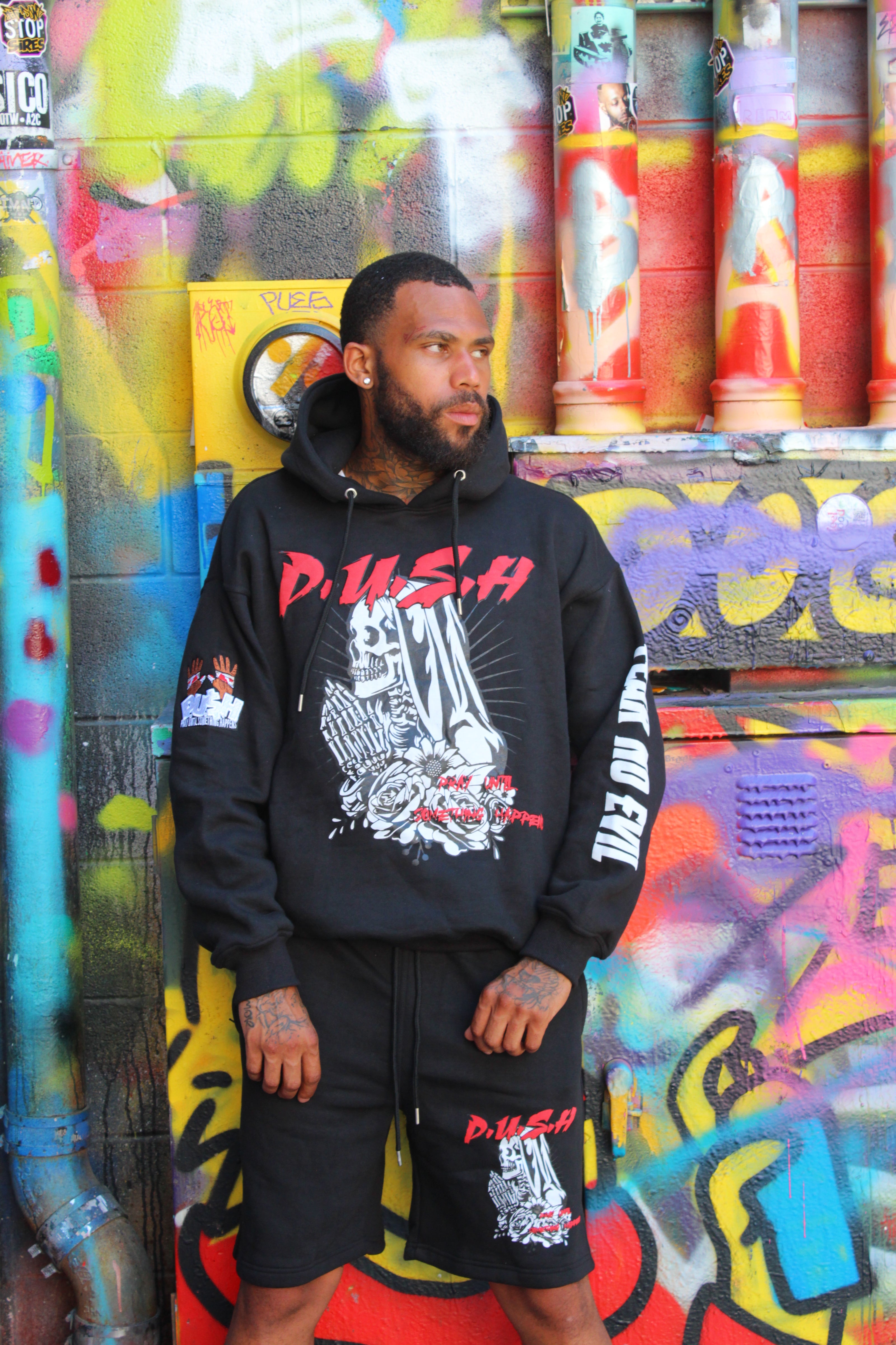 Person wearing a black hoodie with visible branding, standing on a colorful graffiti-covered surface.