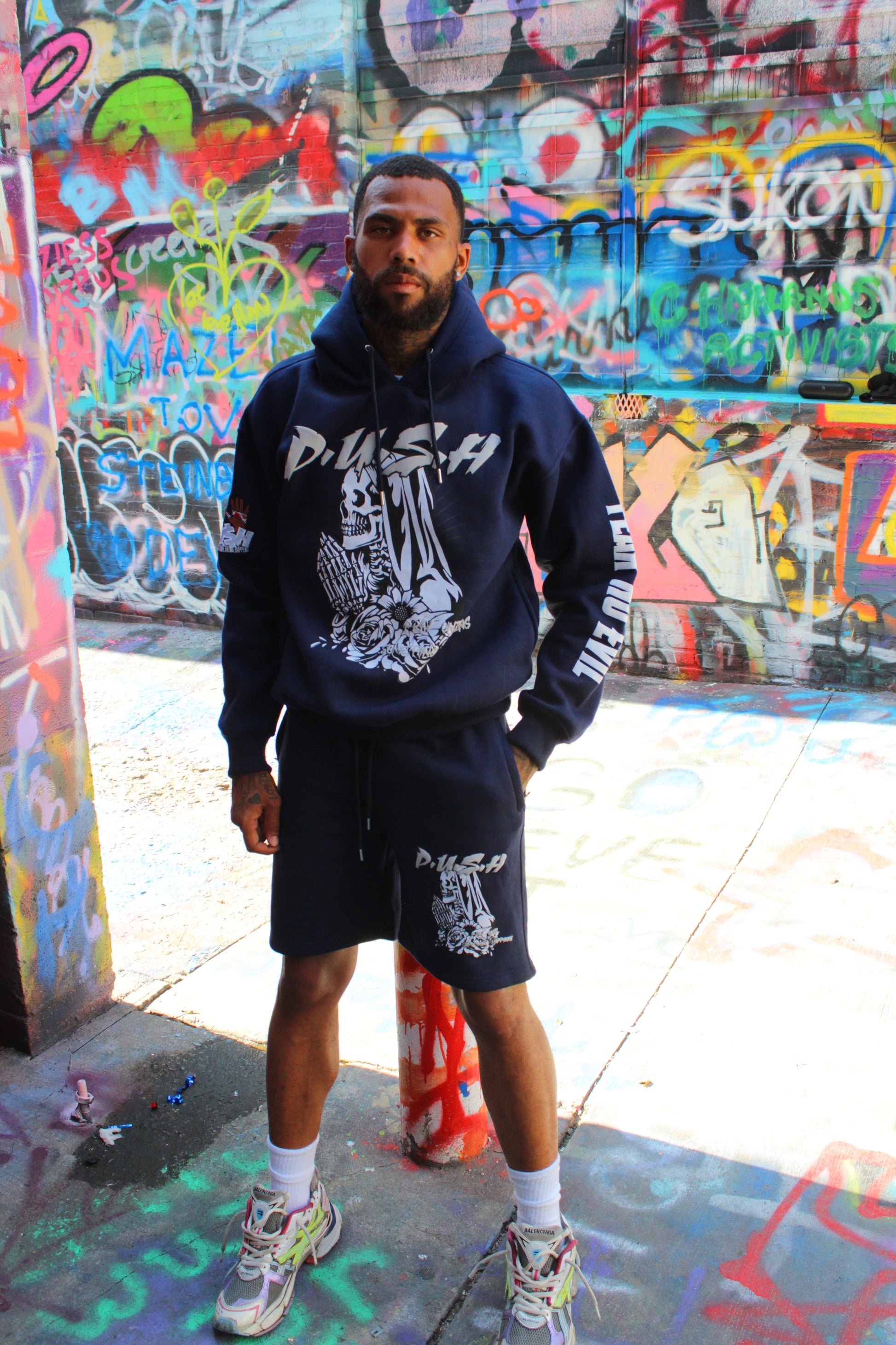 Person wearing a hoodie and shorts standing in front of colorful graffiti